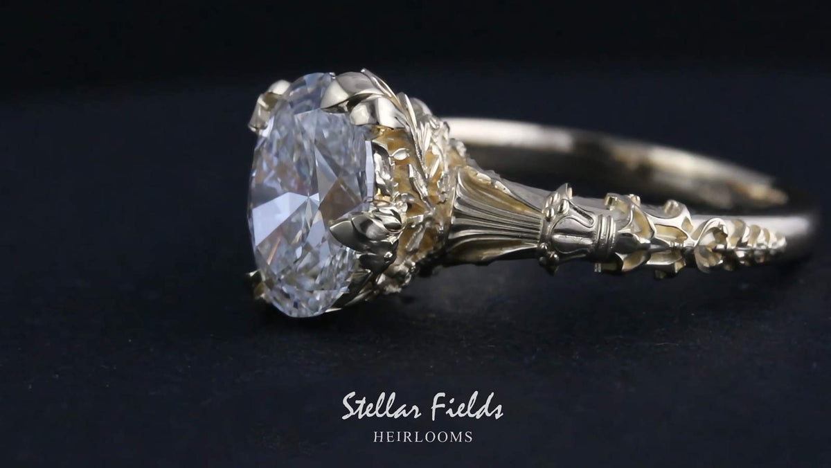 An ornate vintage-style, floral engagement ring featuring a large oval diamond in a detailed gold-toned setting with a matching gold band.  Stellar Fields Jewelry